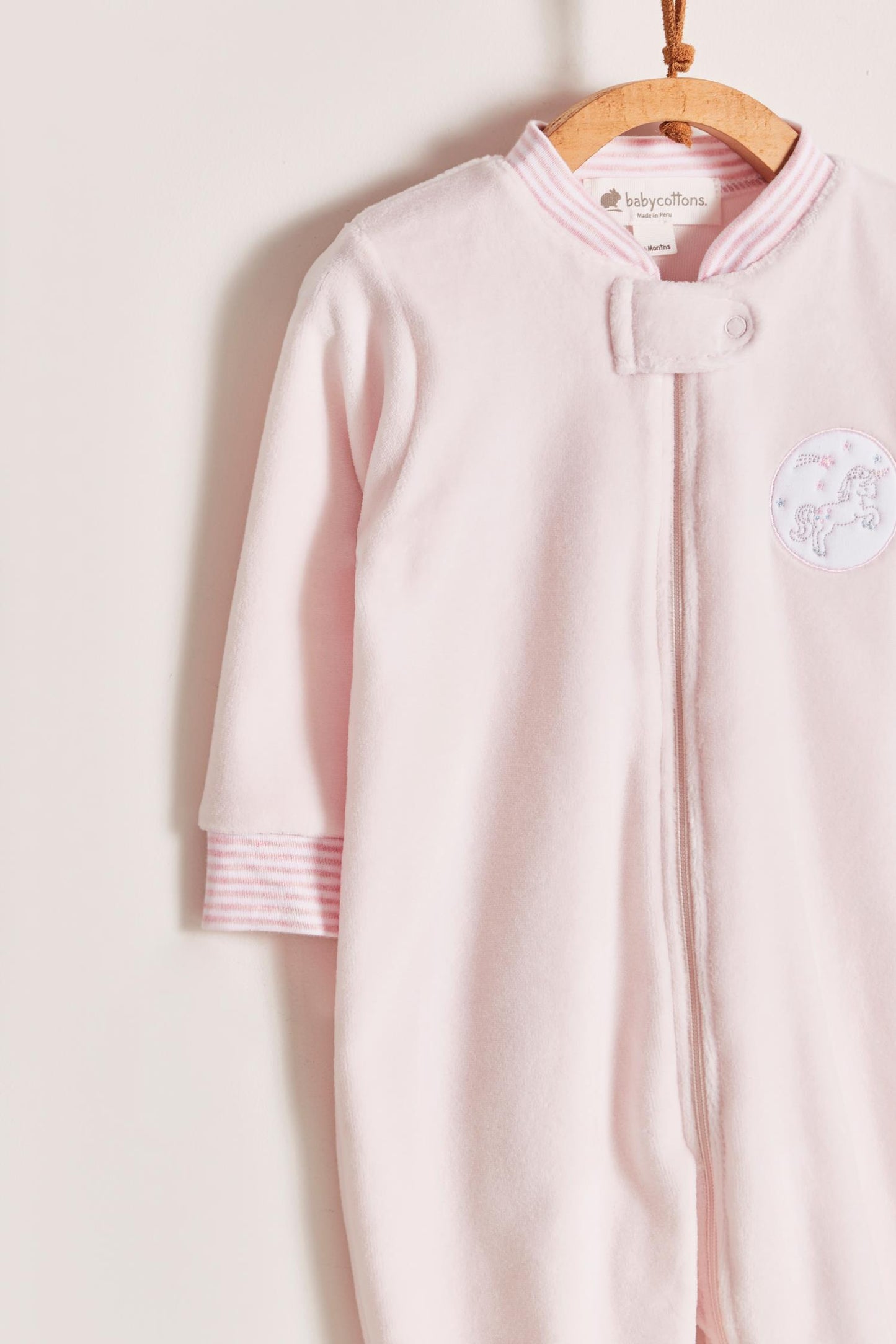 Super warm and soft plush pyjama, ideal to stay warm and comfortable during winter! With long-sleeves, footed and with front closure. Features a lovely striped ribbed collar and cuffs, alongside an embroidered patch on the front. Colour: Pink. Composition: 85% Peruvian Pima cotton, 15% polyester. Made in Peru. Machine washable. Safety warning: Keep away from fire.