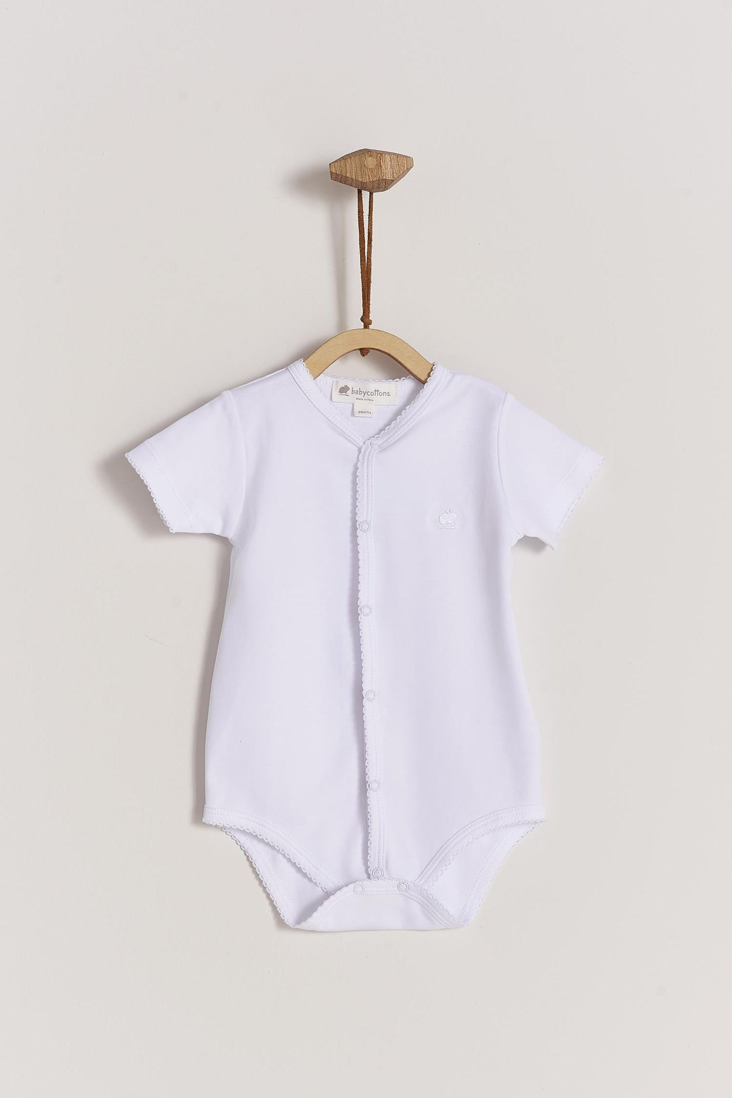 This baby basic short sleeve snapped bodysuit made with 100% super soft and resistant Pima cotton is a must have for your little one. Features a delicate embroidered neckline and sleeves alongside our cute logo bunny embroidered at chest. A baby's wardrobe essential! Popper fastenings around the legs and the front make changing easy, too. Colour: White. Composition: 100% Peruvian Pima Cotton.  Made in Peru.  Machine washable.