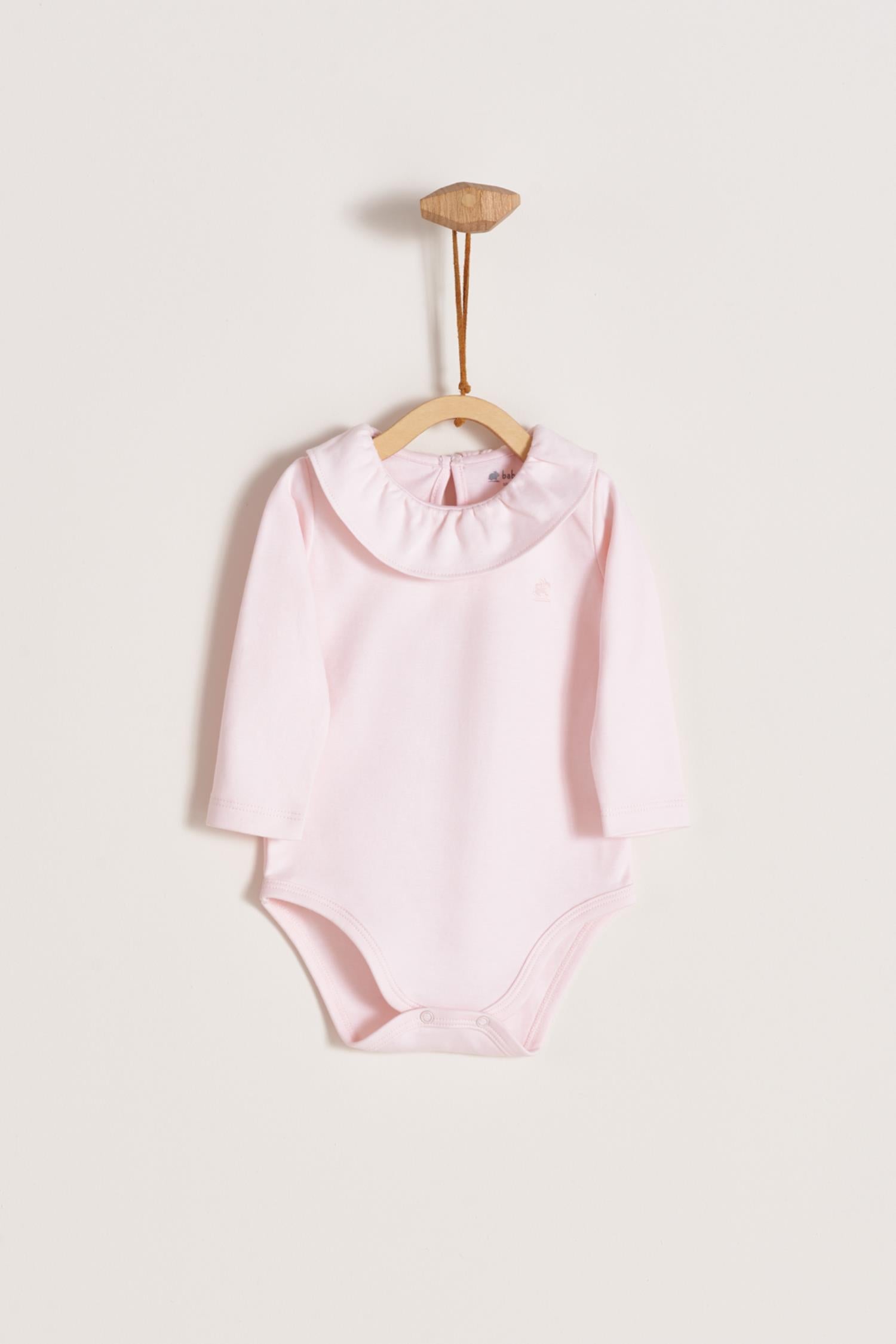 Made from 100% super soft Pima cotton. Long sleeves bodysuit, with cute ruffle collar around.  A classic must have! Popper fastenings around the legs and the back make changing easy, too. Colour: Pink. Composition: 100% Peruvian Pima Cotton.  Made in Peru.  Machine washable.